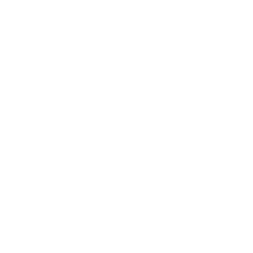 Femme noire de face debout devant un mur rouge avec nuances de gris à côté d'une plante verte dans un pot .Elle porte une combinaison pantalon large avec fines bretelles et col en V avec imprimés colorés africains bleus et oranges. La femme a des lunettes de soleil et a une coupe courte avec macarons violets sur la tête.