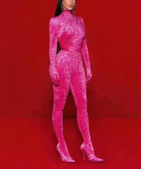 Femme portant une combinaison rose en velours sur un fond rouge.