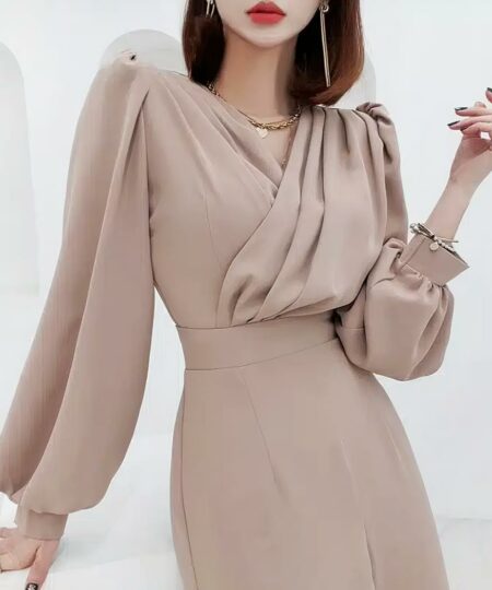 On voit une jeune femme qui porte une magnifique combinaison style smoking beige. L'ensemble est extrêmement sophistiqué et classe. L'encolure du vêtement est plissée et légèrement drapée.
