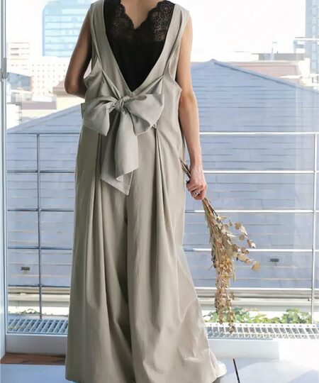 On voit une femme de dos qui porte une combinaison beige nœud avec un bouquet de fleurs.