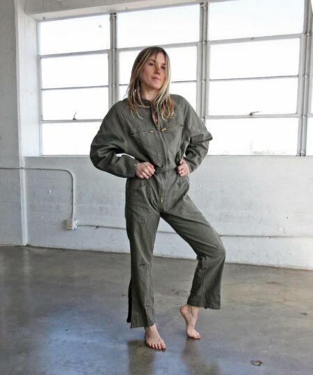 On voit une jeune femme dans un espace vide type loft. Elle porte une combinaison cargo kaki en coton.