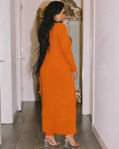 Femme de dos portant une longue combinaison avec un gilet long orange sur un fond blanc.