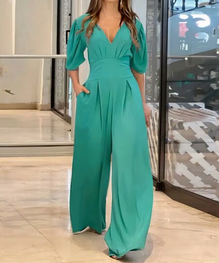 Combinaison verte manches courtes, pantalon fluide, col v, pour modèle féminin mains dans les poches.