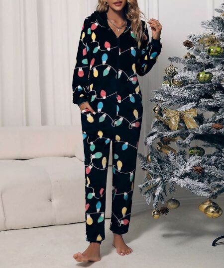 On voit une jeune femme blonde dans un salon blanc, devant un sapin de Noël, qui porte une combinaison en matière polaire noire ornée de guirlandes de toutes les couleurs.