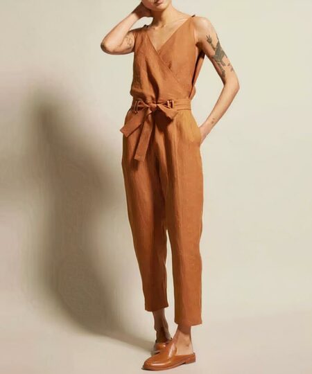 On voit le corps d'une femme sur fond beige. Elle porte une combinaison en lin camel ceinturée à la taille.