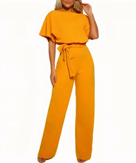 On voit une femme blonde sur fond blanc. Elle porte une élégante combinaison jaune moutarde nouée à la taille.