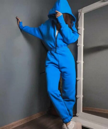 Combinaison pantalon à capuche et zip bleue pour femme qui tient la capuche sur sa tête