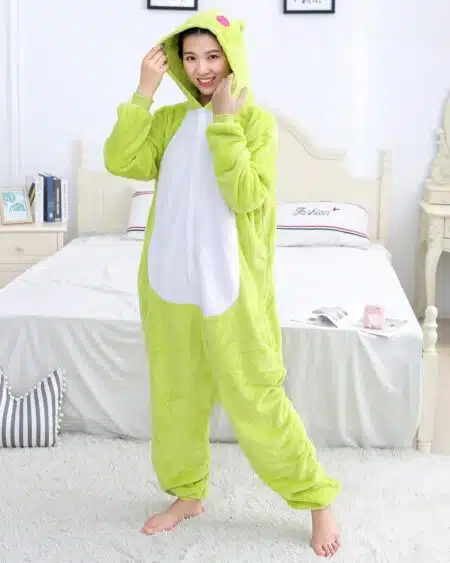 On voit une jeune femme brune dans une chambre scandinave et claire. Elle porte une combinaison pyjama en pilou-pilou verte à l'effigie d'une grenouille.