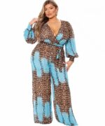 Une femme ronde blonde est debout sur un fond blanc en se caressant les cheveux. Elle porte une combinaison bleu turquoise et imprimé léopard.