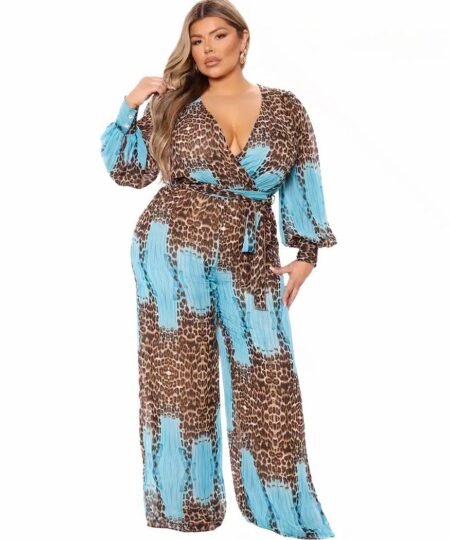 Une femme ronde blonde est debout sur un fond blanc en se caressant les cheveux. Elle porte une combinaison bleu turquoise et imprimé léopard.