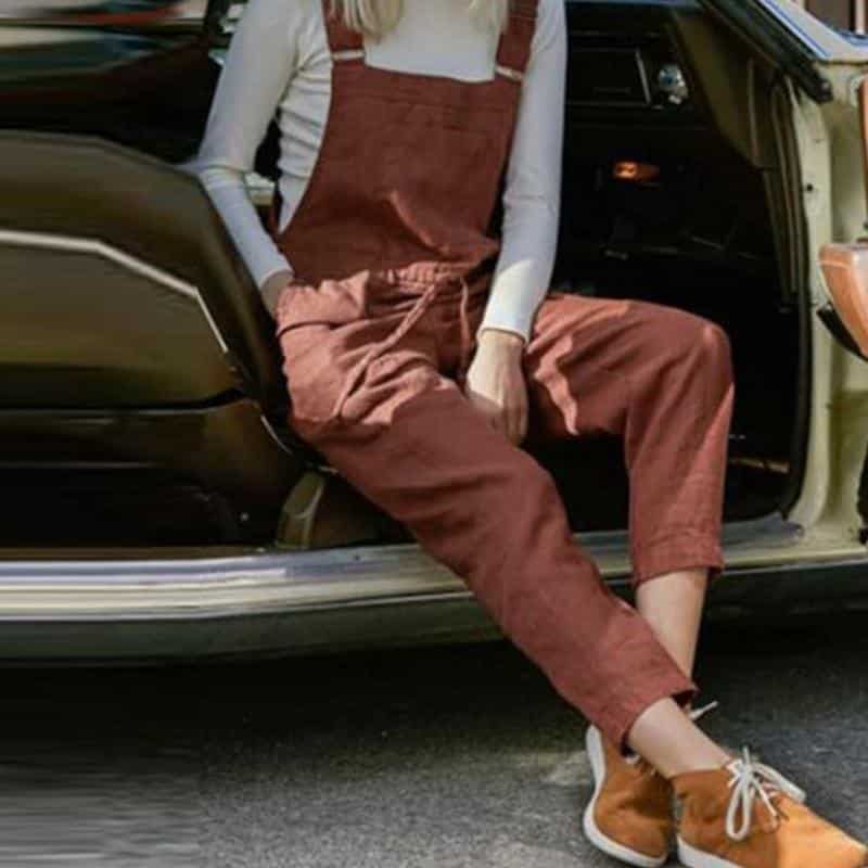 Femme blonde assise à l'avant d'une voiture et portant une combi salopette fluide marron.