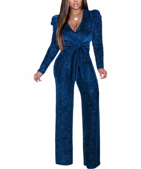 Femme brune sur fond blanc portant une combinaison bleu marine à paillettes.