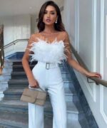 femme portant une combinaison bustier à plumes pour cérémonie blanche avec un sac à main sur des marches d'escalier.
