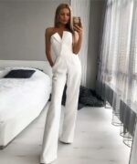 femme portant une combinaison chic blanche se prend en selfie devant un lit blanc dans un appartement