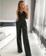 femme portant une combinaison chic noire se prend en selfie dans une chambre devant un lit blanc.