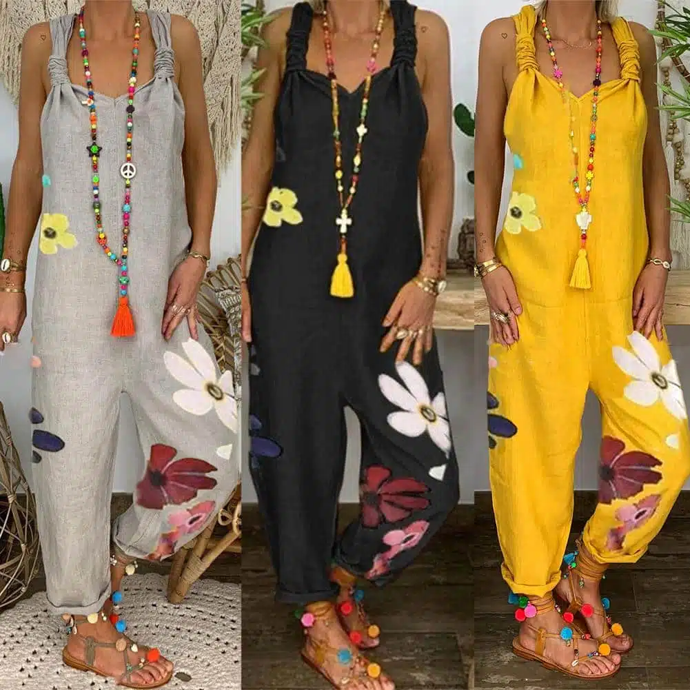 Trois femmes portant une combinaison sarouel sans manches avec imprimé floral en trois coloris : gris, noir et jaune. Elles portent un long collier avec perles et pompons colorés et des sandales à lanières en cuir marron avec pompons multicolores.