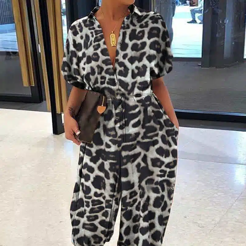 Femme dans un hall portant une combinaison sarouel léopard noir avec une pochette marron dans la main.