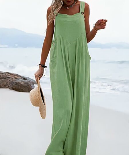 On voit une femme sur la plage. Elle porte une combinaison ample vert pale et un chapeau de paille à la main.