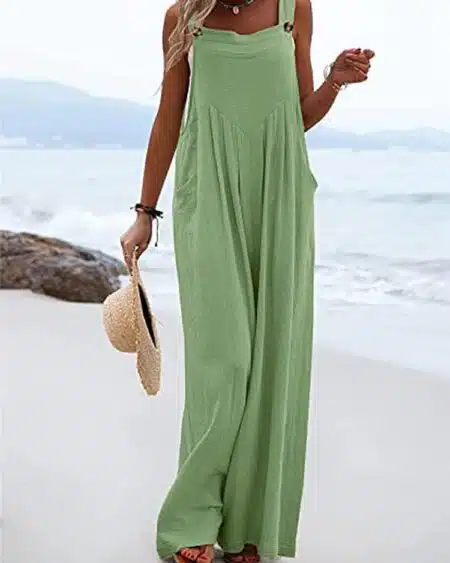 On voit une femme sur la plage. Elle porte une combinaison ample vert pale et un chapeau de paille à la main.