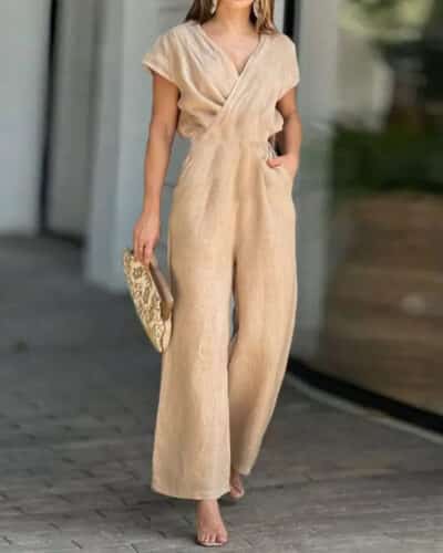 On voit une femme qui marche dans la rue, près d'une vitrine, et qui porte une combinaison en lin avec un décolleté en V. La combinaison est beige.
