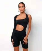 femme métisse cheveux courts debout devant un mur blanc les bras le long du corps avec le mains sur ses cuisses portant une combinaison de fitness asymétrique et moulante qui ne descend jusqu'à ses genoux.