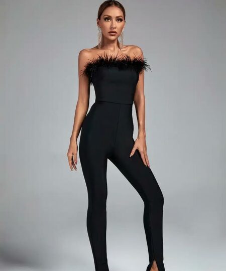 femme portant une combinaison de soirée chic à plumes noire avec des talons au pieds prend la pose les bras le long du corps devant un mur gris et sur un sol gris