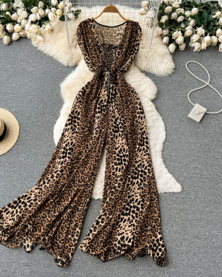 combinaison ample été à imprimé léopard pour femme étendu sur du coton blanc, sur une table gris avec un chapeau, un collier et des fleurs blanches autour.
