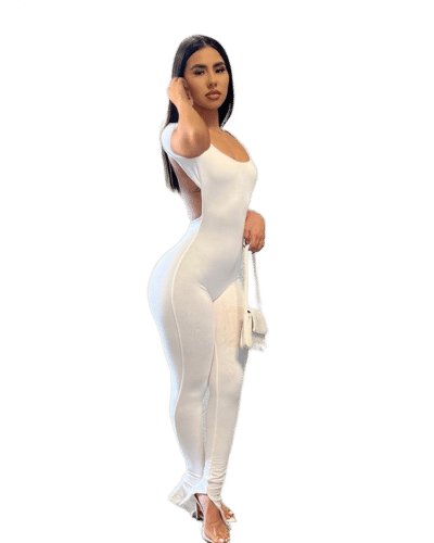 femme portant combinaison dos nu chic en coton blanche avec un sac à mains et des talons tout en se touchant les cheveux