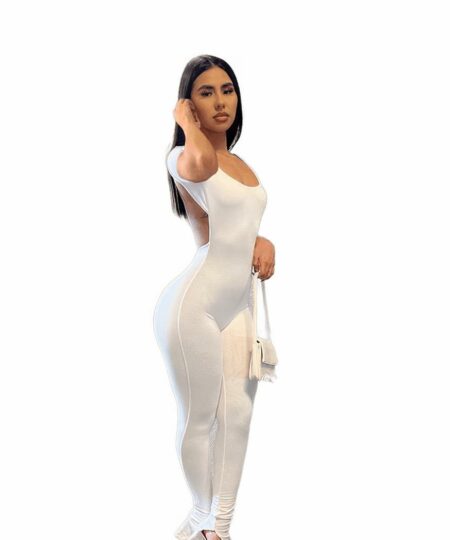 femme portant combinaison dos nu chic en coton blanche avec un sac à mains et des talons tout en se touchant les cheveux