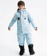 Combinaison de ski enfant épaisse et imperméable avec une capuche portée par un petit garçon avec des bottes noires sur fond gris