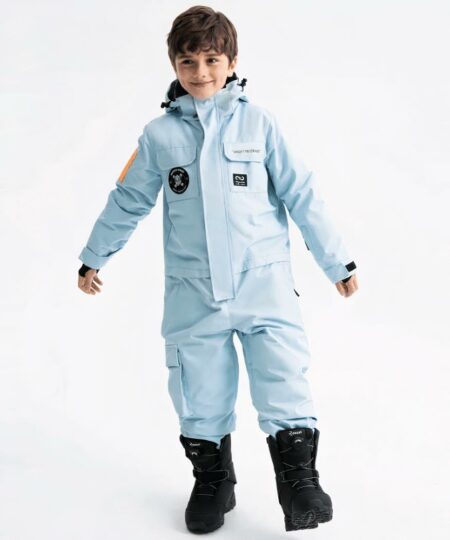Combinaison de ski enfant épaisse et imperméable avec une capuche portée par un petit garçon avec des bottes noires sur fond gris