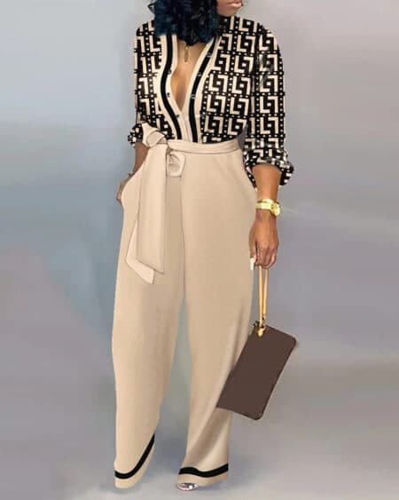 une femme pose devant un fond gris elle porte un sac a main dans sa main elle a une combinaison pantalon bi couleur noir et beige et elle est brune