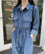 haut de jambes et buste de femme en combinaison côtelé bleue, elle a les mains dans ses poches et elle est devant la devanture d'un magasin